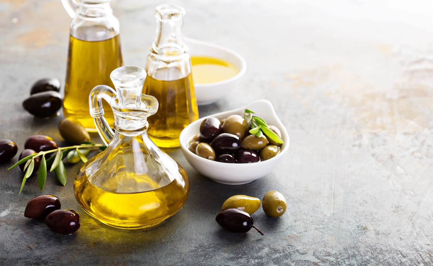 Olivenöl in Karaffen neben Schale voll mit Oliven
