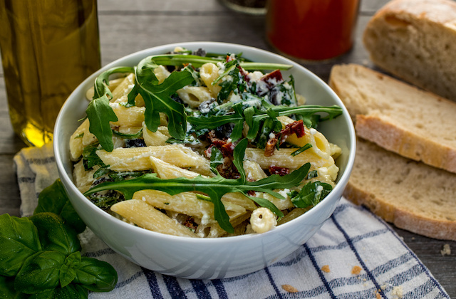 Mediterraner Nudelsalat mit getrockneten Tomaten und Rucola angerichtet in Schüssel mit Baguette