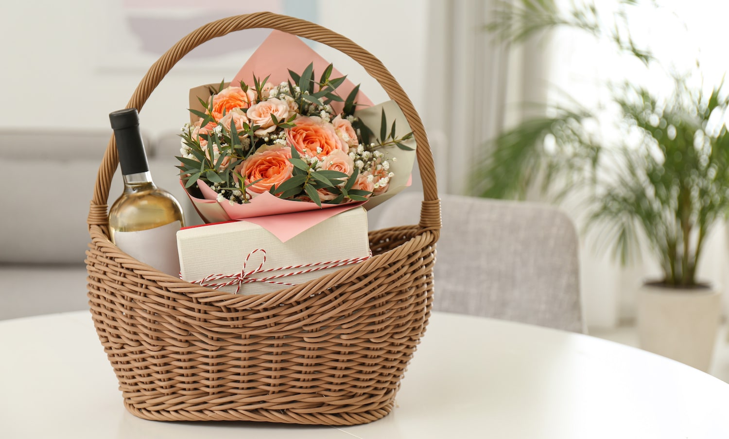Geschenkkorb mit Blumen und Weißwein auf Tisch