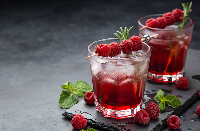 Himbeer Rosen Eistee im Glas mit Eiswürfeln, Minze und Himbeerspieß