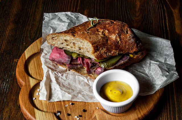 Pastrami Sandwich mit Essiggurken und Café de Paris Dip auf Holzbrett