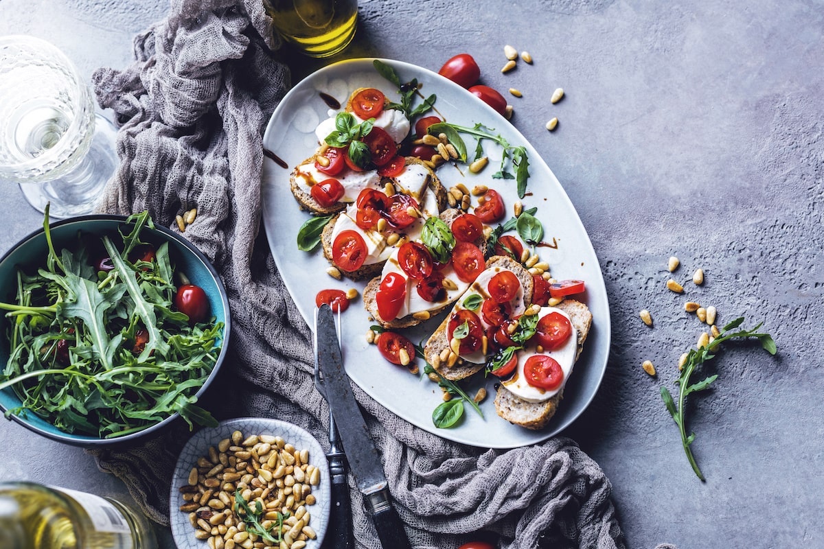 Bruschetta mit Tomate, Mozzarella, Rucola und Pinienkernen auf Teller