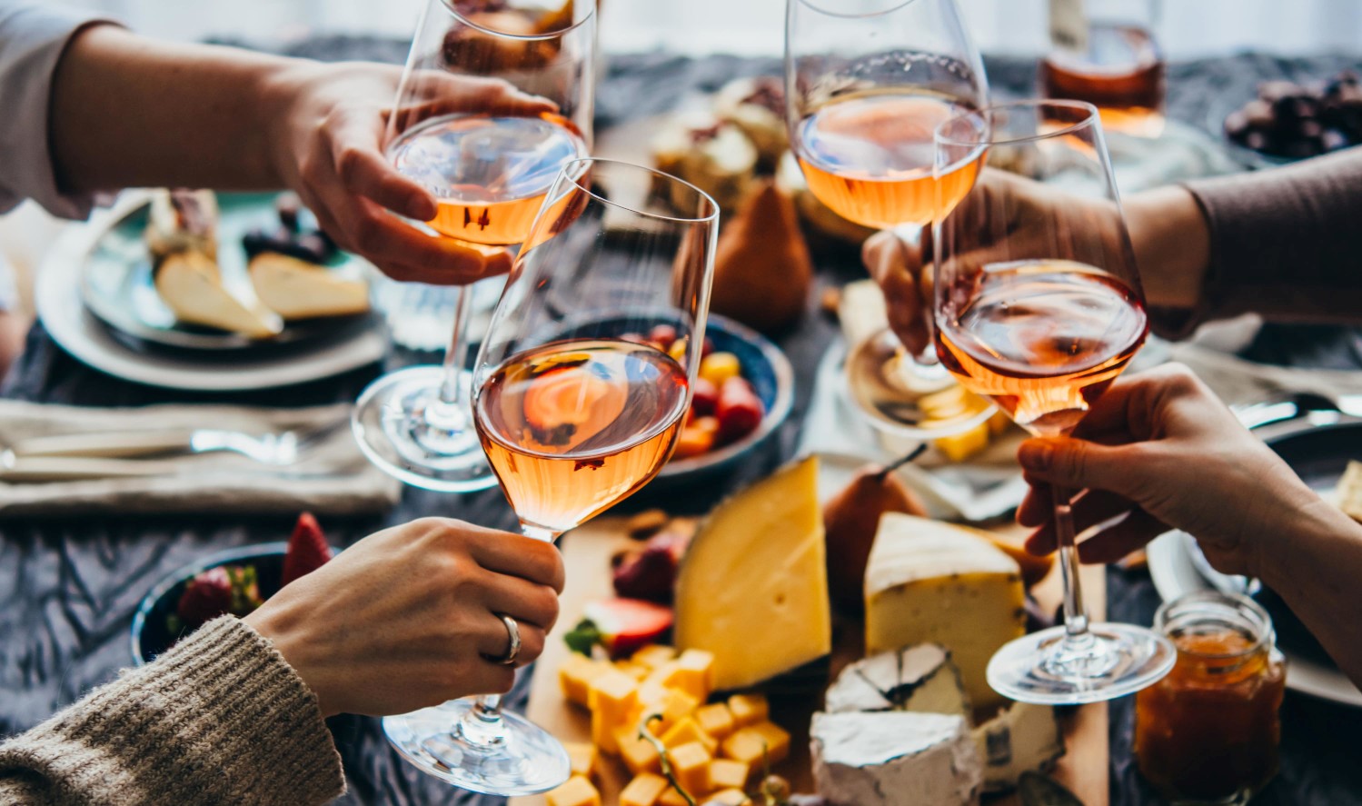 Vier Personen stoßen mit Rosé Wein an an einem Tisch mit einer Käseplatte