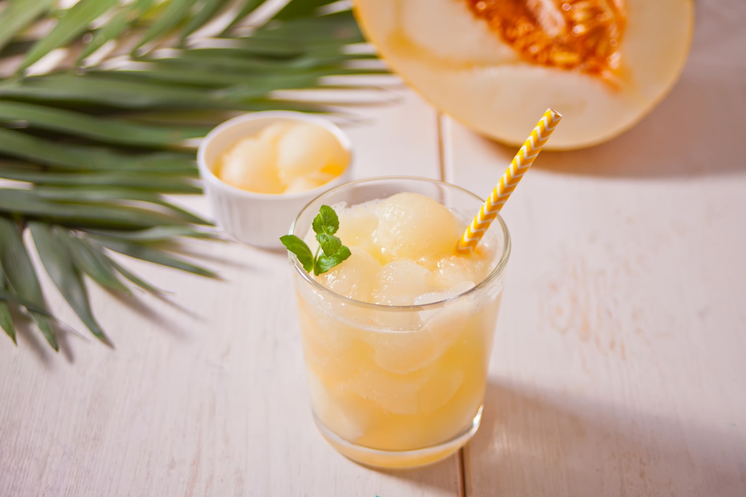 Cocktail mit Melonenlikör und Honigmelone im Glas neben Palmblatt