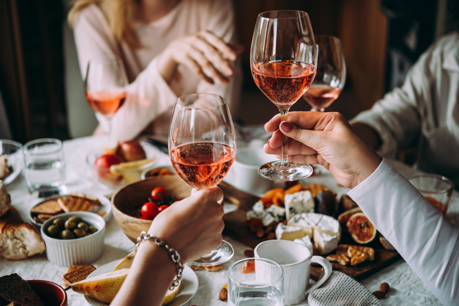 Frauen, die mit Rosé Wein anstoßen , an einem Tisch mit Käseplatte, Tomaten, Oliven und mehr
